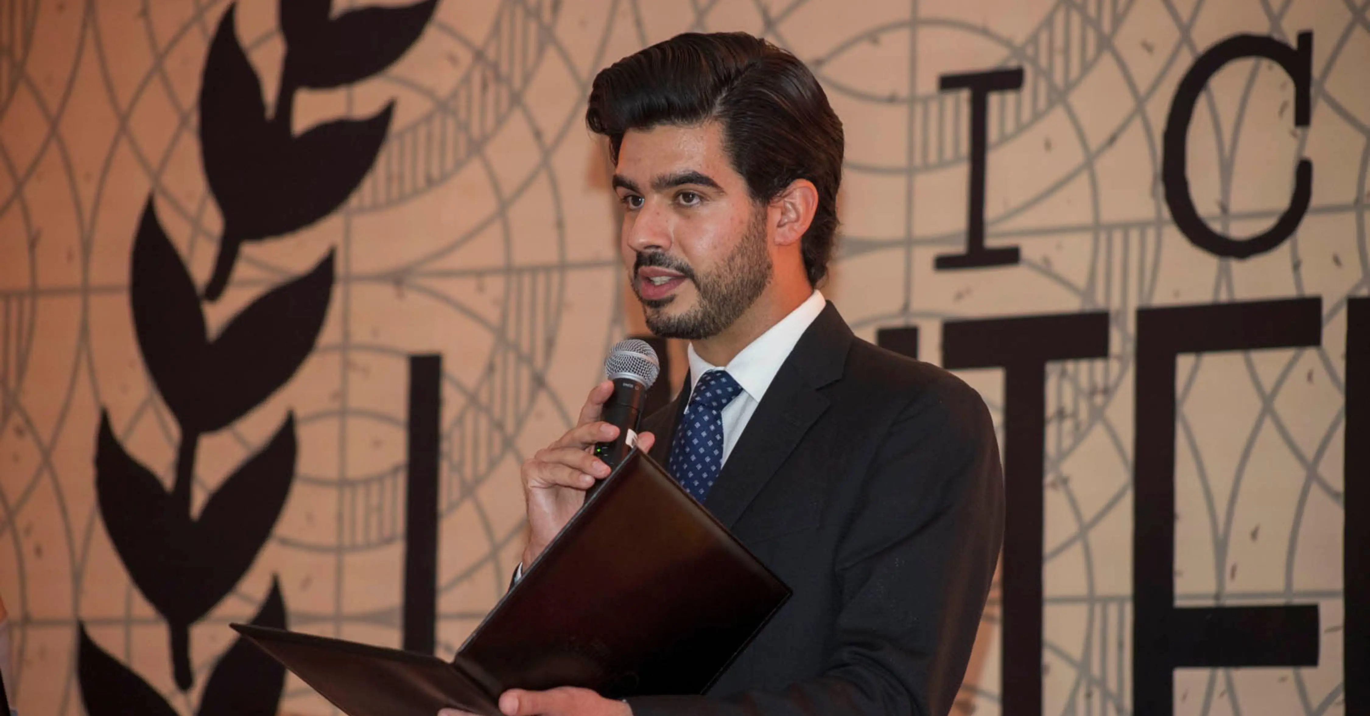 Estudiante de la anáhuac con traje dando un discurso diplomático frente a un foro