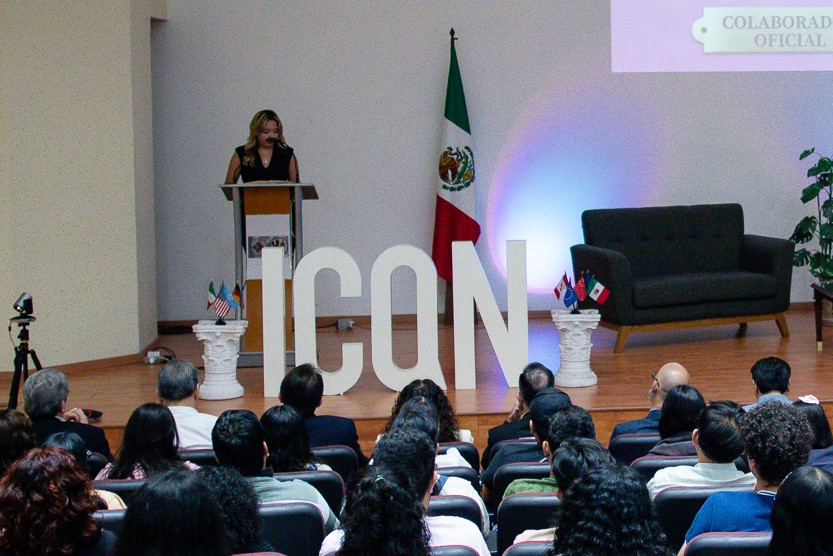 Imagen del escenario de ICON: una alumna como maestra de ceremonias y todo el público le presta atención.