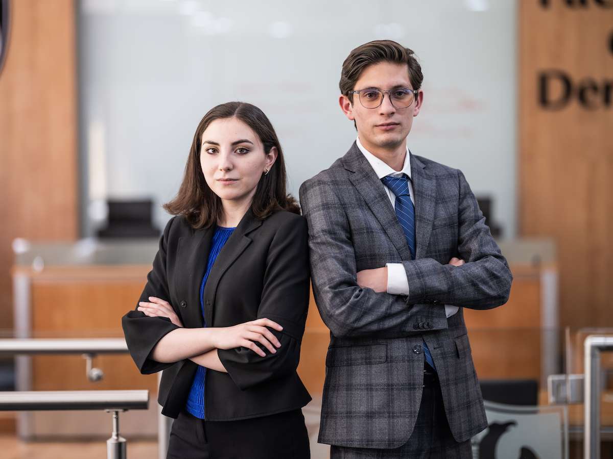 Estudiantes de Derecho posando con los brazos cruzados en una sala tipo tribunal, proyectando seguridad, profesionalismo y compromiso con la formación jurídica.