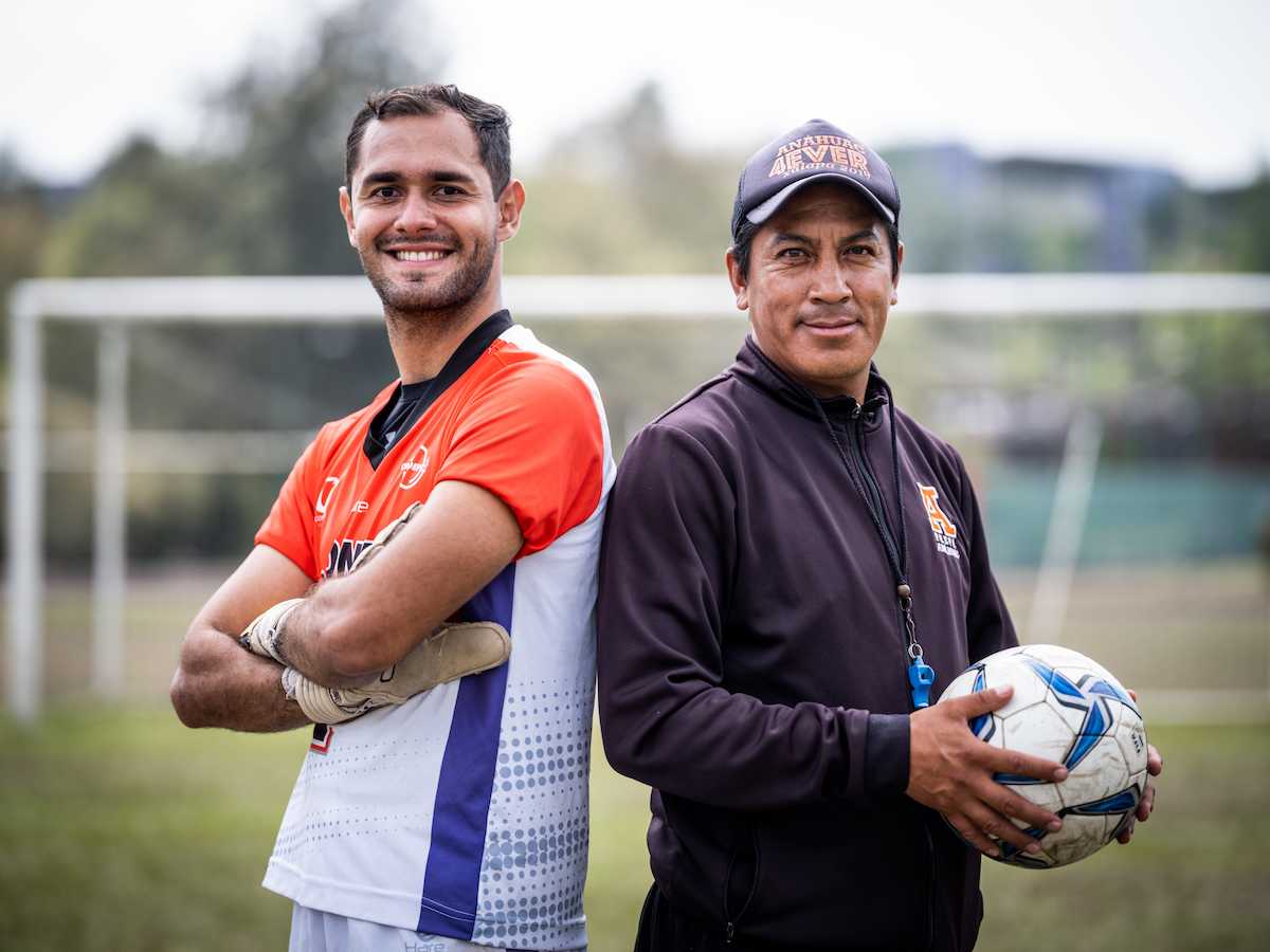 Jugador de fútbol y entrenador posando juntos en el campo de entrenamiento con balón.