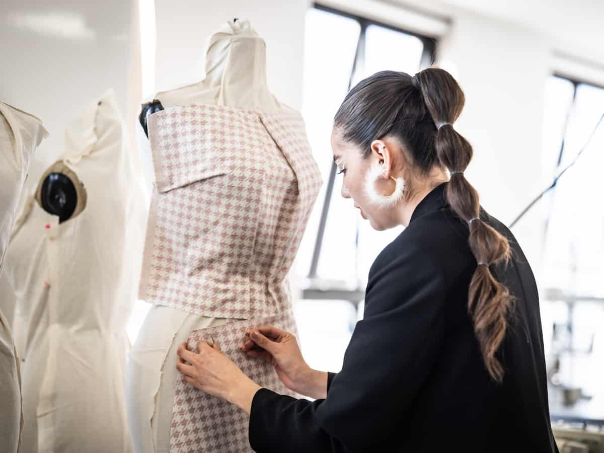 Diseñadora realizando prueba de entalle con tela de cuadros sobre maniquí durante proceso de creación de prenda.