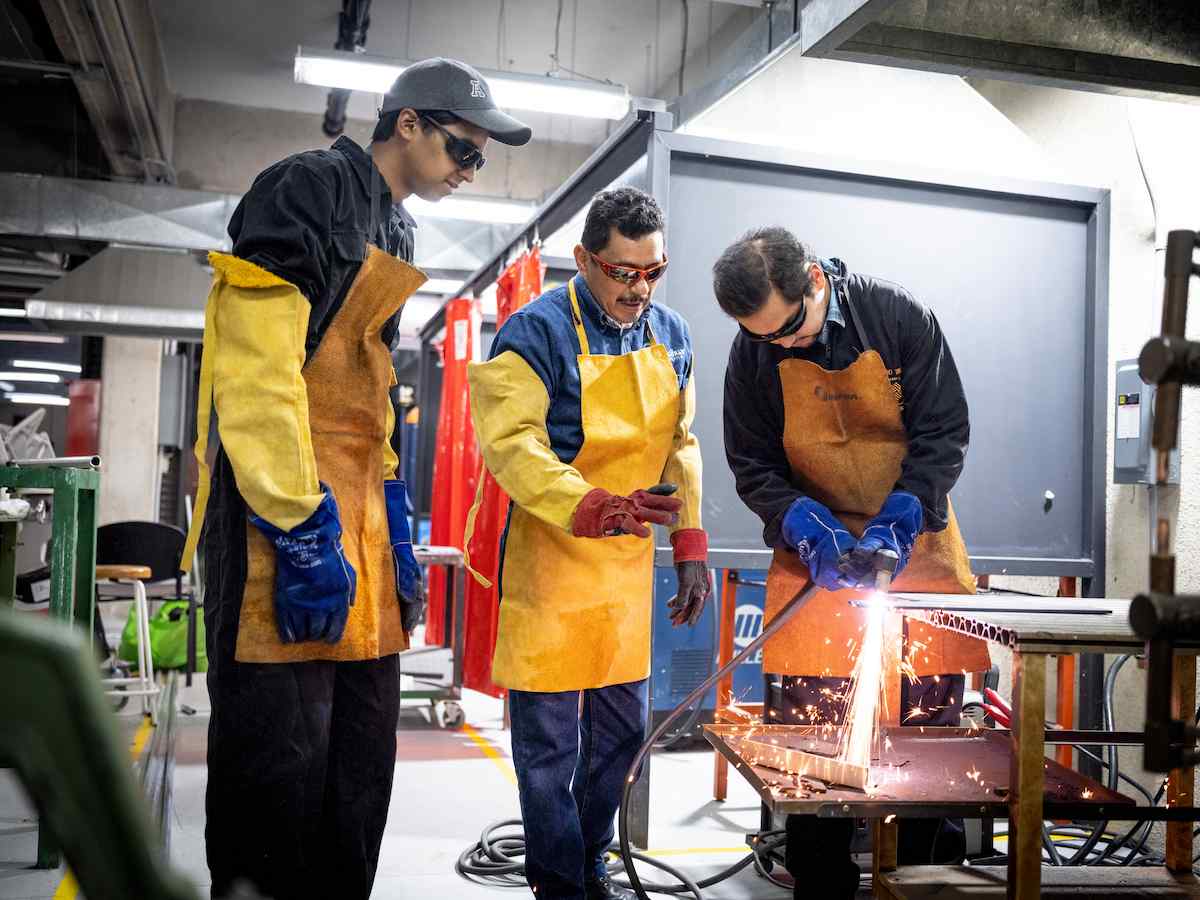 Tres personas con equipo de seguridad realizan práctica de corte con soplete, generando chispas sobre mesa metálica en taller industrial.