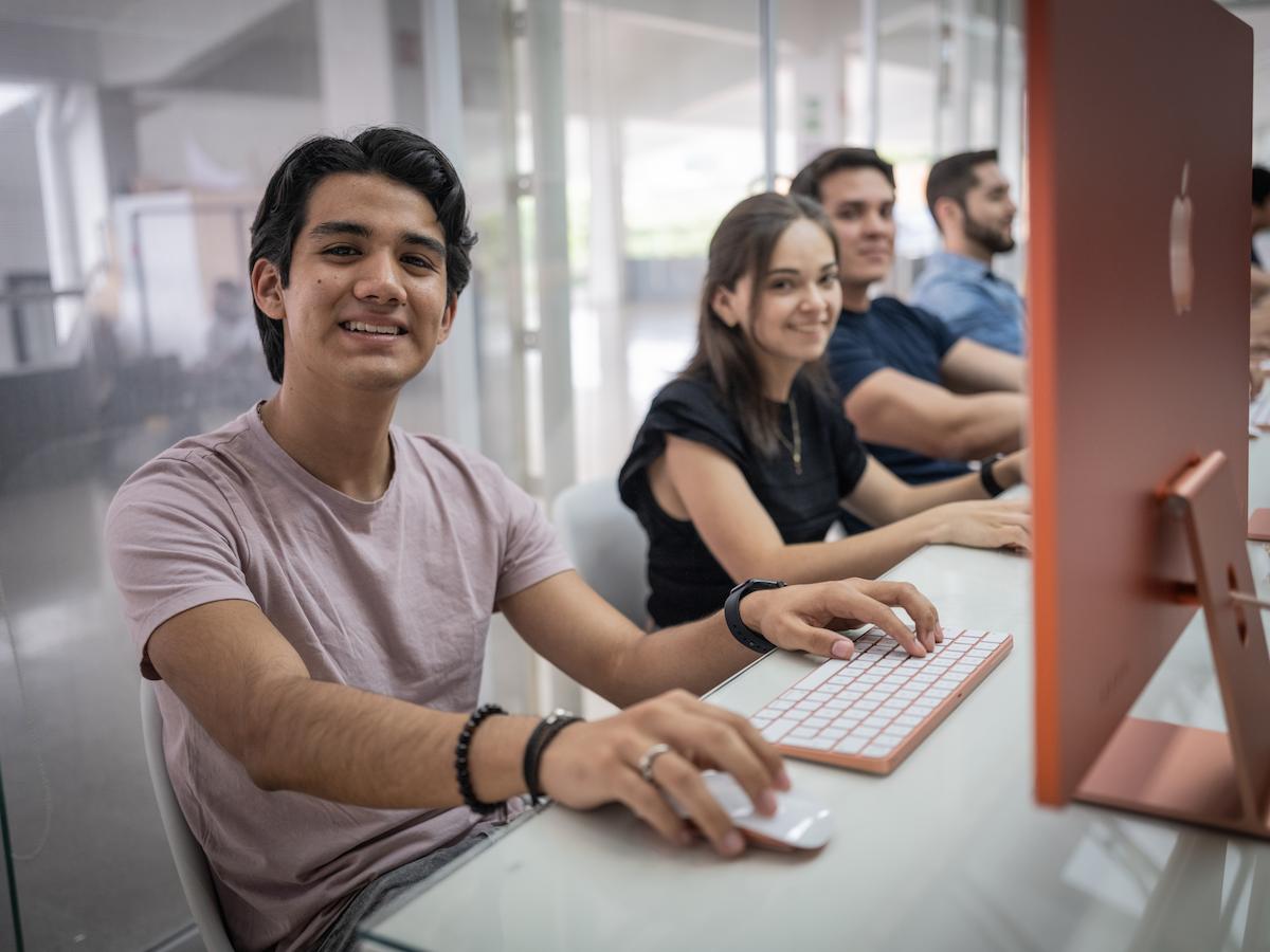 Grupo de estudiantes usando computadoras Apple en un espacio luminoso, reflejando un entorno de aprendizaje tecnológico y colaborativo.